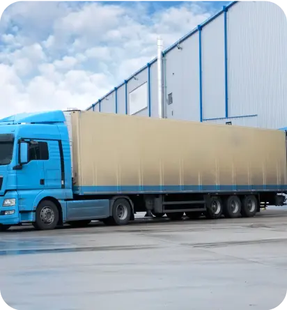 Duża niebieska ciężarówka wyjeżdżająca z magazynu – nawiązanie do branży transportowej.